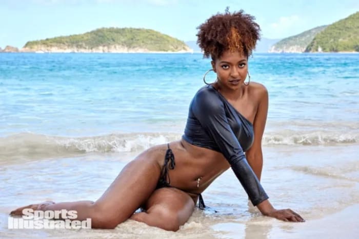 DiDi Richards sits in the incoming tide in a black latex top and a pair of black string bottoms.